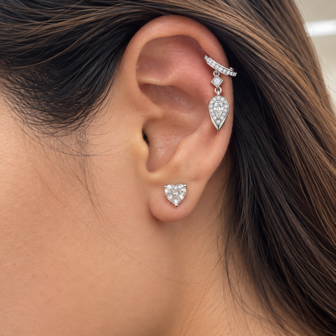  model wearing a white gold lab-grown diamond ear cuff with pavé-set diamonds, a dangling pear-cut diamond halo charm, and a heart-shaped lab-grown diamond stud earring.

